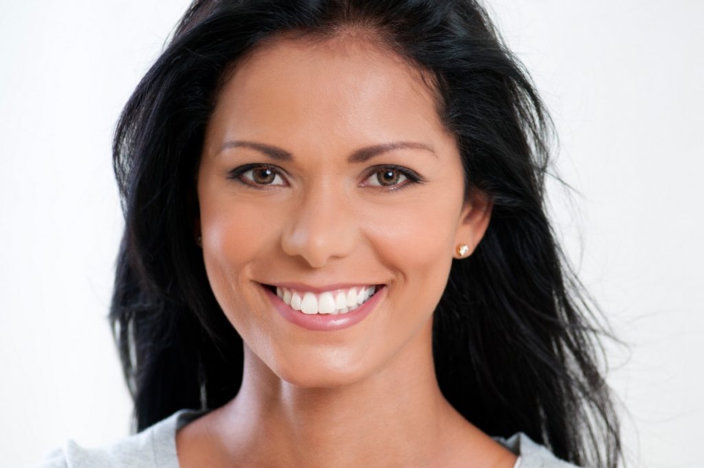 Rosto de mulher de cabelos pretos, sorrindo com dentes saudáveis e brancos