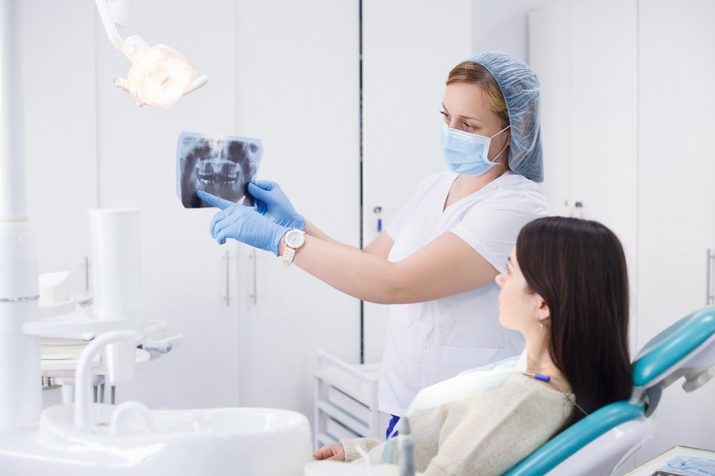 No consultório odontológico, a dentista mostra os detalhes do exame radiológico para a paciente que está sentada na cadeira.